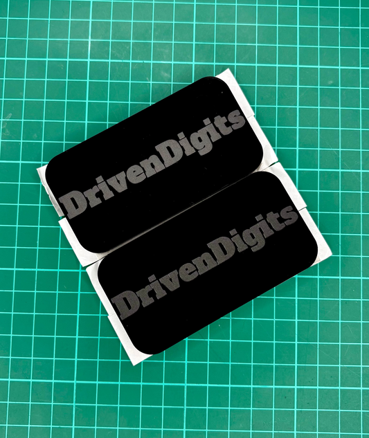 Two black 'DrivenDigits' magnets on a green grid background