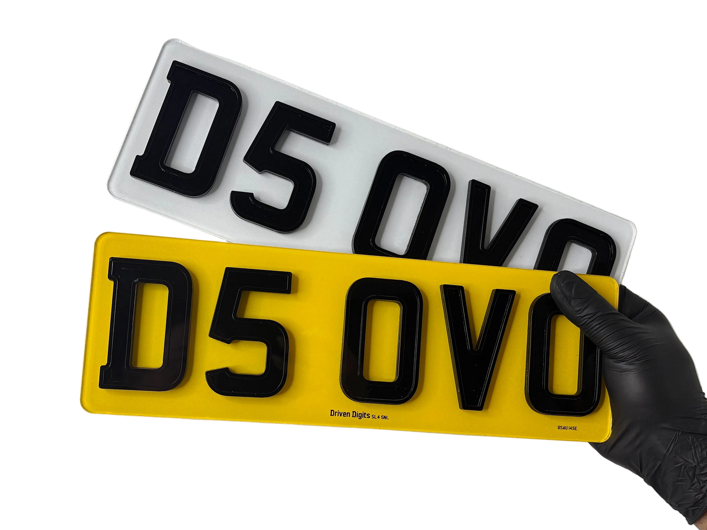 Two shortened ghost number plates, one yellow and one white with black text, held by a gloved hand on a white background.