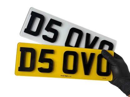 Two shortened ghost number plates, one yellow and one white with black text, held by a gloved hand on a white background.