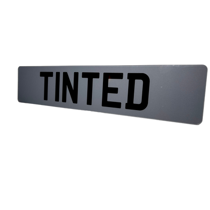 Rectangular gray sign with 'TINTED' in black text on a white background