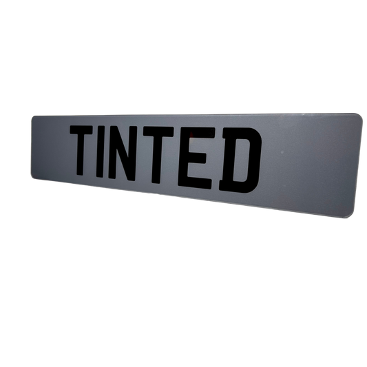 Rectangular gray sign with 'TINTED' in black text on a white background